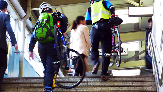 自転車を担いで階段を昇り、モノレール乗り場へと向かう参加者たち（11月30日、千葉モノレール実証実験「サイクル＆モノレール」）