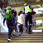 自転車を担いで階段を昇り、モノレール乗り場へと向かう参加者たち（11月30日、千葉モノレール実証実験「サイクル＆モノレール」）